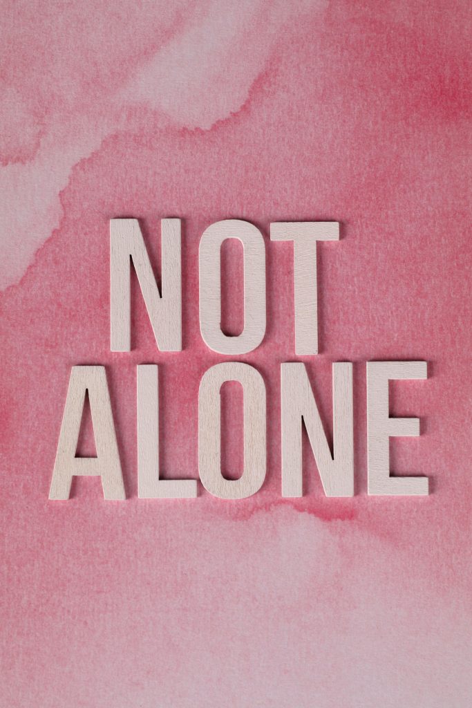 Text 'Not Alone' on pink watercolor background conveying support and unity.